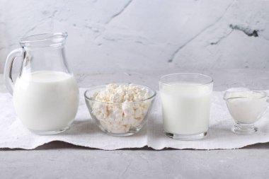 Süt ürünleri: süt, kefir veya ayran, şeffaf bir kâsede süzme peynir ve ekşi krema, gri arka planda sürahi ve cam, yatay yönelim