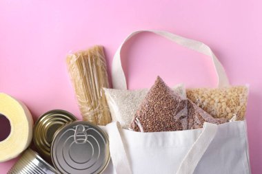 Gıda teslimatı, Bağış, Tekstil Market Torbası. Pembe arka planda karantina için gıda stokları. Pirinç, karabuğday, makarna, konserve yiyecek, tuvalet kağıdı, Top view