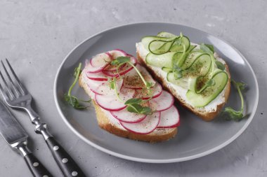 Gri beton arka planda gri tabakta salatalıklı, turplu ve bezelyeli iki sandviç.