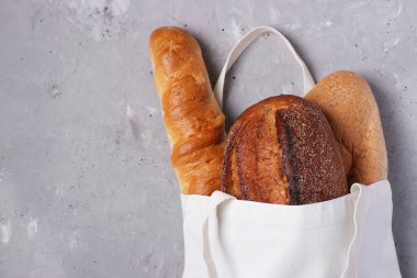 Gri beton arka planda taze ekmek bulunan el yapımı pamuk tekstil alışveriş torbası. Sıfır atık, çevre dostu alışveriş ve ekoloji konsepti. Üst Görünüm, Boşluğu Kopyala