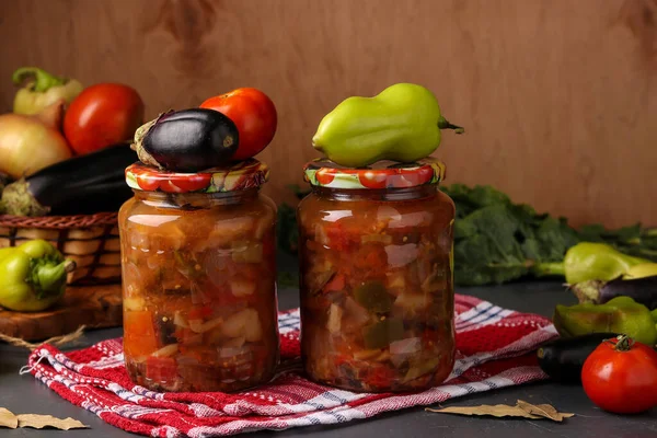 Patlıcan, biber, soğan ve domatesli sebze salatası. Cam kavanozlarda, tahta masada, yatay formatta, yakın plan.