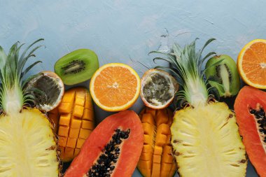 Tropikal meyvelerin yarısı: papaya, mango, ananas, kivi, turuncu ve tutku meyvesi açık mavi arka planda, Üst Manzara, Yatay Biçim