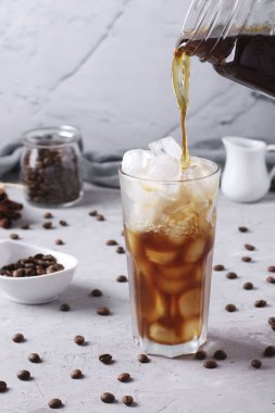 Açık gri zemin üzerinde buz küpleri olan uzun bardağa soğuk kahve doldurmak, ferahlatıcı içecek, dikey format