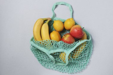 Sarı olgun muzlar, limonlar ve elmalar yeniden kullanılabilir ağ torbasının içinde turkuaz renk açık arkaplanda, sıfır atık konsepti, Üst görünüm