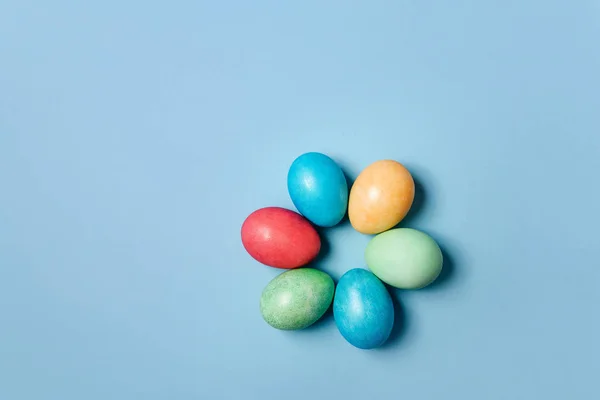 Colored easter eggs lie in the shape of a flower on a blue background.