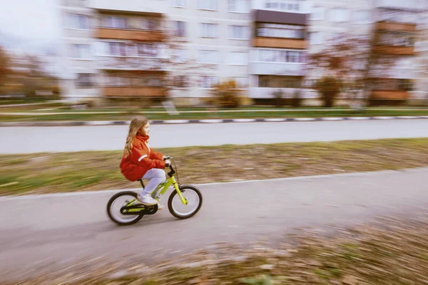 Young blonde girl in red jacket riding bike — Stock Photo, Image