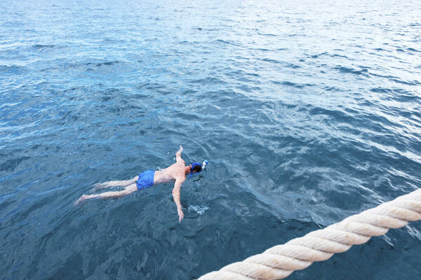 Young man in swimwear lying in blue water, aerial view
