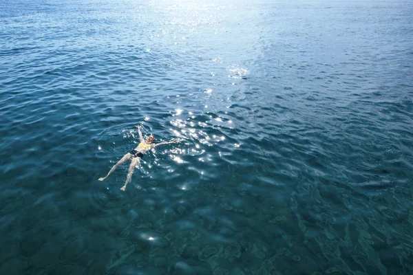 Młoda kobieta w strojach kąpielowych leżąca na błękitnej wodzie, widok z powietrza — Zdjęcie stockowe