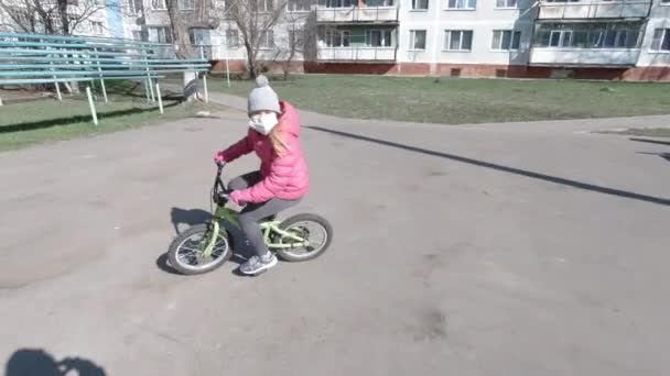 Jong blond meisje in roze jas paardrijden fiets — Stockvideo