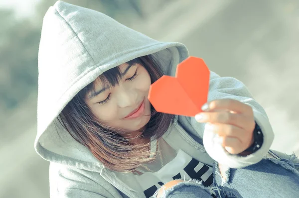 Happy pretty shy young female holding red heart paper