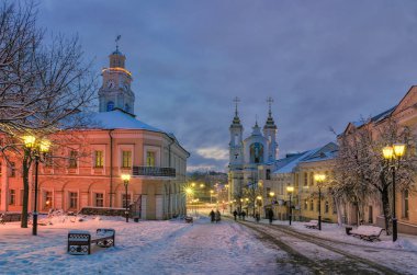 Eski Avrupa şehrinin sokağında, kış sabahının erken saatlerinde. Eski evler ve kilise. Işıklar hala açık.