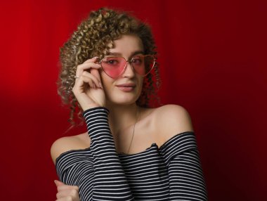 Sarı kıvırcık saçlı, pembe gözlüklü genç kız. 