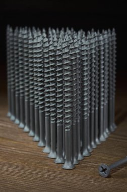 Gri kendi kendine dokunan vidalar ahşap bir masa üzerinde bir üçgen şeklinde durur, yanında bir vida, çerçeve dikey oryantasyon