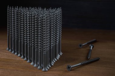 Gri kendi kendine dokunan vidalar ahşap bir masanın üzerinde üçgen şeklinde, yanında da birkaç vida var, yakın plan. Üstteki sağ kısım yazma için ücretsizdir