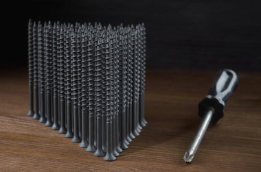 Gri kendi kendine dokunan vidalar, tahta bir masanın üzerinde, bir tornavidanın yanında bir üçgen şeklindedir..