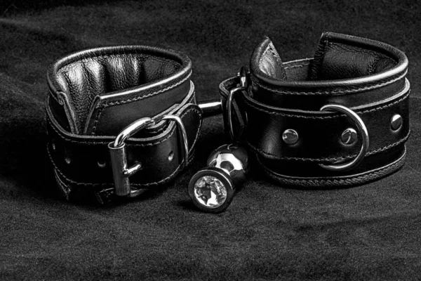 Leather handcuffs and anal plug on black background. — Stock Photo, Image