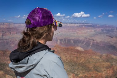Arkadan mor başlıklı kız, Büyük Kanyon 'u görüyor, kızıl uçurumlar, güneş ve mavi gökyüzü, ABD