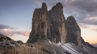 Dolomite Alpleri 'ndeki milli parktaki Paternsattel' den hareketli bulutlarla dolu renkli günbatımında Three Peaks 'in zaman akışı, öndeki kayalar, yazları kar, Güney Tyrol İtalya