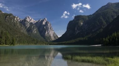 Dolomite Alplerinde Toblacher Gölü 'nün zamanaşımı güneşli bir günde, mavi gökyüzü, hareket eden bulutlar, plajdaki insanlar, Güney Tyrol İtalya