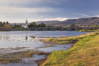 Köprü Ponte de Lima Kilisesi, güneşli bir günde öğleden sonra, nehir kenarında Lima Nehri ve nehir kenarında yeşil çimenler.