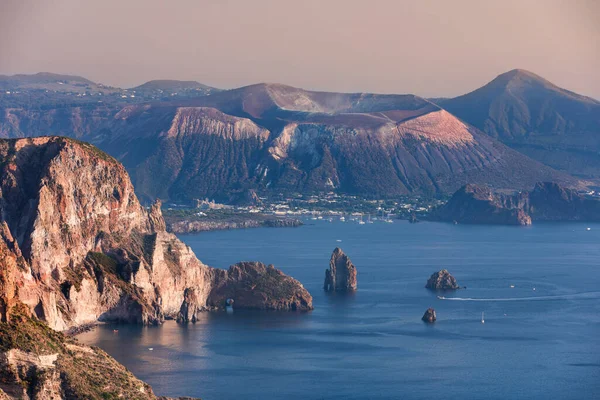Lipari adasının kıyı şeridi, gün batımında Volkan adası manzaralı, Vulcano, kayalıklar ve okyanus, su üzerinde kayıklar, Sicilya İtalya