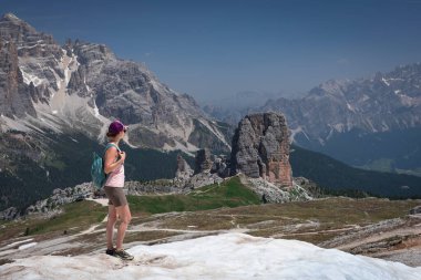 Yaz mevsiminde Dolomite Alpleri 'nde Cinque Torri' nin önünde kar tarlasında yürüyüş yapan sırt çantalı ve şortlu bir kadın.