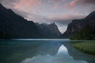 Toblach Gölü, günbatımında su yüzeyindeki Dolomite Alp Dağları 'nın yansımaları, gökyüzündeki renkli bulutlar, sabah sisi, Güney Tyrol İtalya