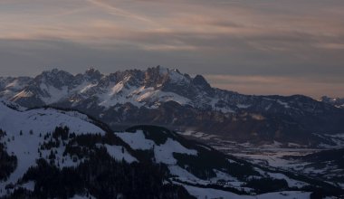 Fieberbrunn 'daki dağlık Wilder Kaiser dağları. Kışın gün batımında kar, orman ve vadi, gökyüzünde bulutlar, Tyrol Avusturya.