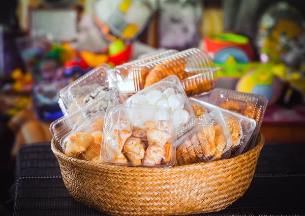 Plastic wegwerp verpakkingen met koekjes en gebak in een rieten houten mand op een bonte, gekleurde achtergrond — Stockfoto