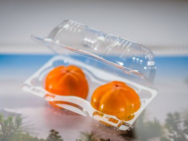 Persimmons in a transparent plastic disposable container on a li clipart