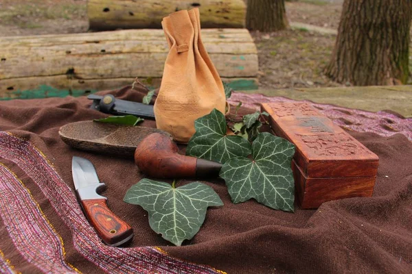 Still Life - a knife, wooden pipe, box and a poach arranged on a table in a garden with ivy leaves