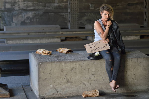 alcohol addicted, homeless woman with emptied bottled alcohol in brown paper bags next to her begging for money holding a sign - are you my neighbor? 