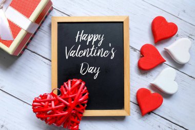 Kırmızı ahşap el sanatları kalp simgesi, bir hediye kutusu ve 'Happy Valentine'S Day ile' yazılı yazı tahtası beyaz beyaz ahşap arka plan üzerinde top. Valentine's day Tema.