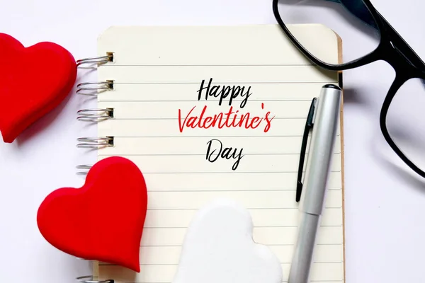 開かれた本のペンとサングラスで 幸せなバレンタインの日 と書かれている白い木製背景上赤と白の木製手芸ハートマークの平面図です バレンタインの日のテーマ — ストック写真