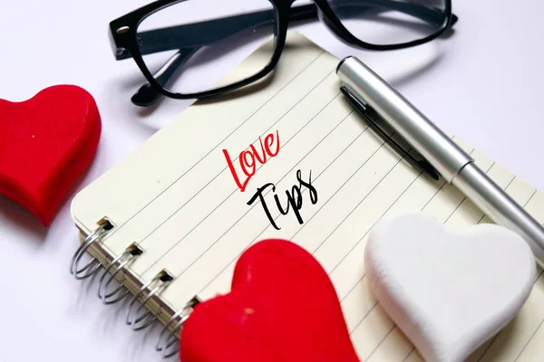 Kırmızı ve Beyaz ahşap üstten görünüm Elişi kalp simgesi, kalem ve sunglass 'Aşk İpuçları' beyaz arka plan ile yazılmış açık bir kitap üzerinde. Valentine's day Tema.