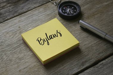 Compass,pen and yellow sticky notes written with Bylaws on wooden background. clipart