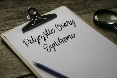 Magnifying glass,pencil and clipboard with white paper written with Polycystic Ovary Syndrome on wooden background. clipart