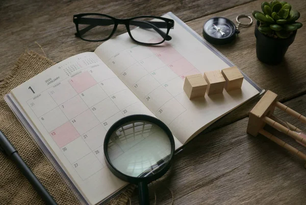 Ovanifrån av januari 2020 planerare med glasögon, kompass, växt, sand klocka, förstoringsglas, och penna på trä bakgrund. — Stockfoto