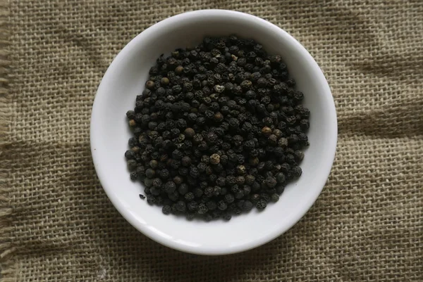 Pimienta negra en un plato blanco en un saco de alfombra . —  Fotos de Stock