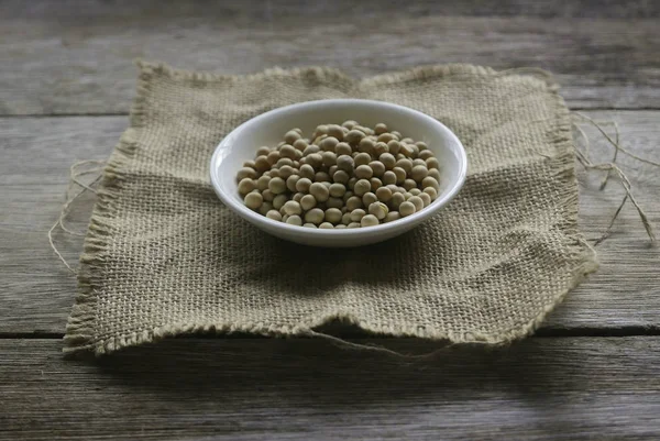 Soja en un plato blanco sobre un saco de alfombra sobre fondo de madera . —  Fotos de Stock