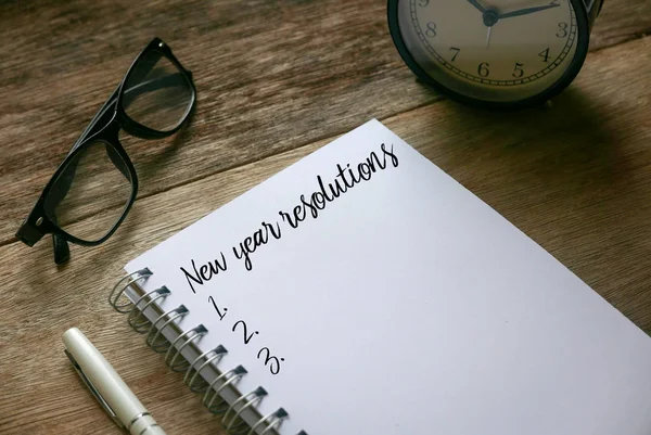 Ovanifrån av penna, klocka, solglasögon och anteckningsbok skriven med nyårslöften på trä bakgrund. — Stockfoto