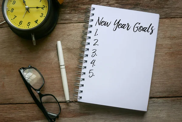 Κάτοψη του στυλό, γυαλιά ηλίου, ρολόι και σημειωματάριο γραμμένο με το Νέο Έτος Στόχοι σε ξύλινο φόντο. — Φωτογραφία Αρχείου