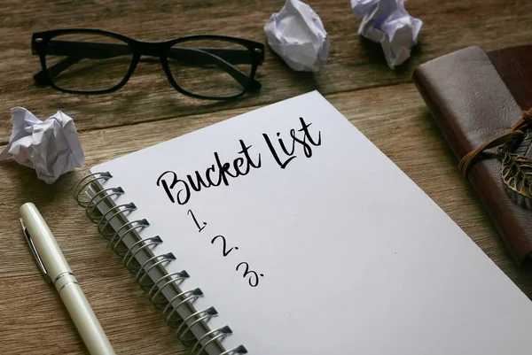 Stylo, papier poubelle, lunettes de soleil et carnet écrit avec Bucket List sur fond en bois . — Photo