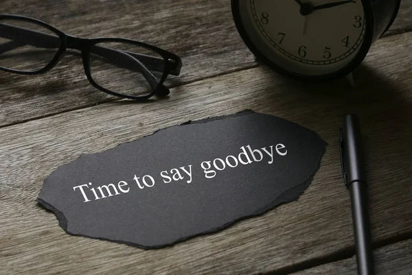 Óculos, relógio, caneta e um pedaço de papel preto escrito com Time to say goodbye on wooden background . — Fotografia de Stock