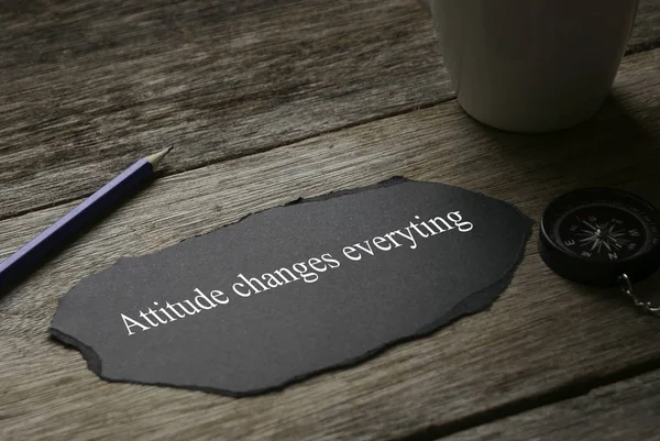 Une tasse, une boussole, un crayon et un morceau de papier noir écrit avec Attitude Changes Everything sur fond en bois . — Photo