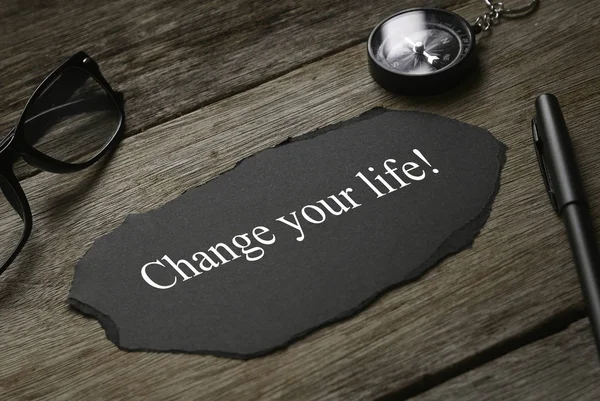 Kompas, bril, pen en stukje zwart papier geschreven met Change Your Life! op houten ondergrond. — Stockfoto