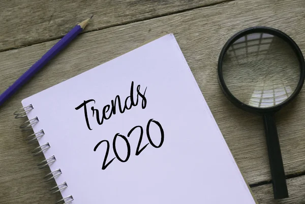 Vista superior de lupa, lápis e caderno escrito com Trends 2020 sobre fundo de madeira . — Fotografia de Stock