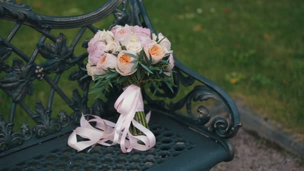 Bouquet de mariage de roses et pivoines sur un banc en métal noir à l'ancienne décoré de vignes en métal. Bouquet nuptial de différentes fleurs. Bouquet de belles fleurs roses, crème et blanches — Video