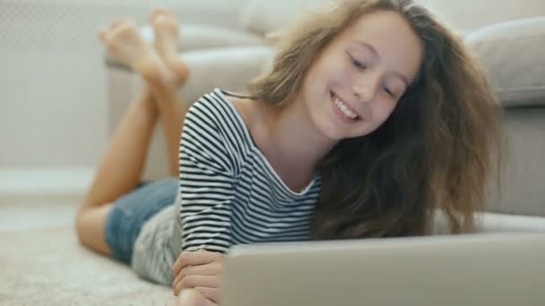 カーペットの上の十代の少女は、ノート パソコンから読んでいます。. — ストック動画