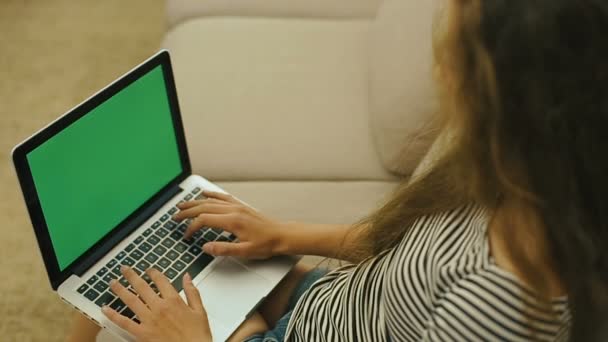 Menina adolescente em um sofá está trabalhando com um laptop, pesquisando na web. Menina adolescente com laptop está sorrindo para a câmera. Tela verde. Steadicam tiro . — Vídeo de Stock